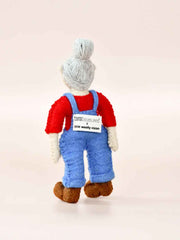 Felt toy figure wearing a red shirt and blue overalls on a light pink background