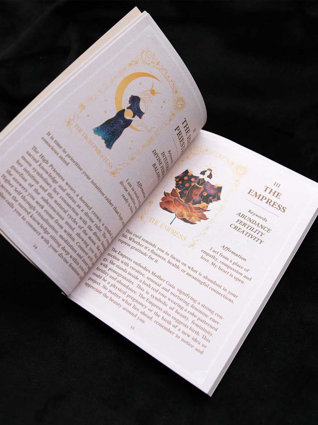 An open book spread photographed from above on a black fabric background. The pages are cream-colored with printed text and decorative illustrations, including a crescent moon and star motif on one page and a floral illustration on the other.
