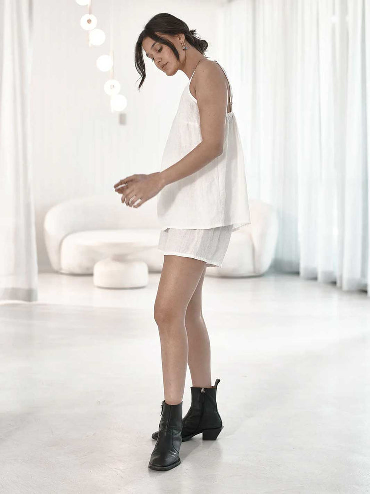 Woman in a white outfit with black boots standing in a minimalistic room.