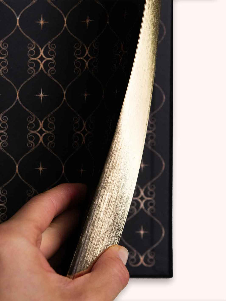 Hand holding gold gilded pages against a black background with gold patterns