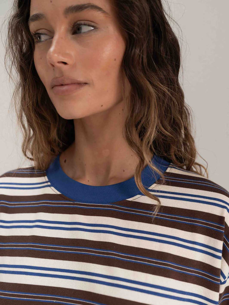 A close-up of a woman wearing a striped crewneck t-shirt with brown, cream, and blue horizontal stripes and a solid blue collar.