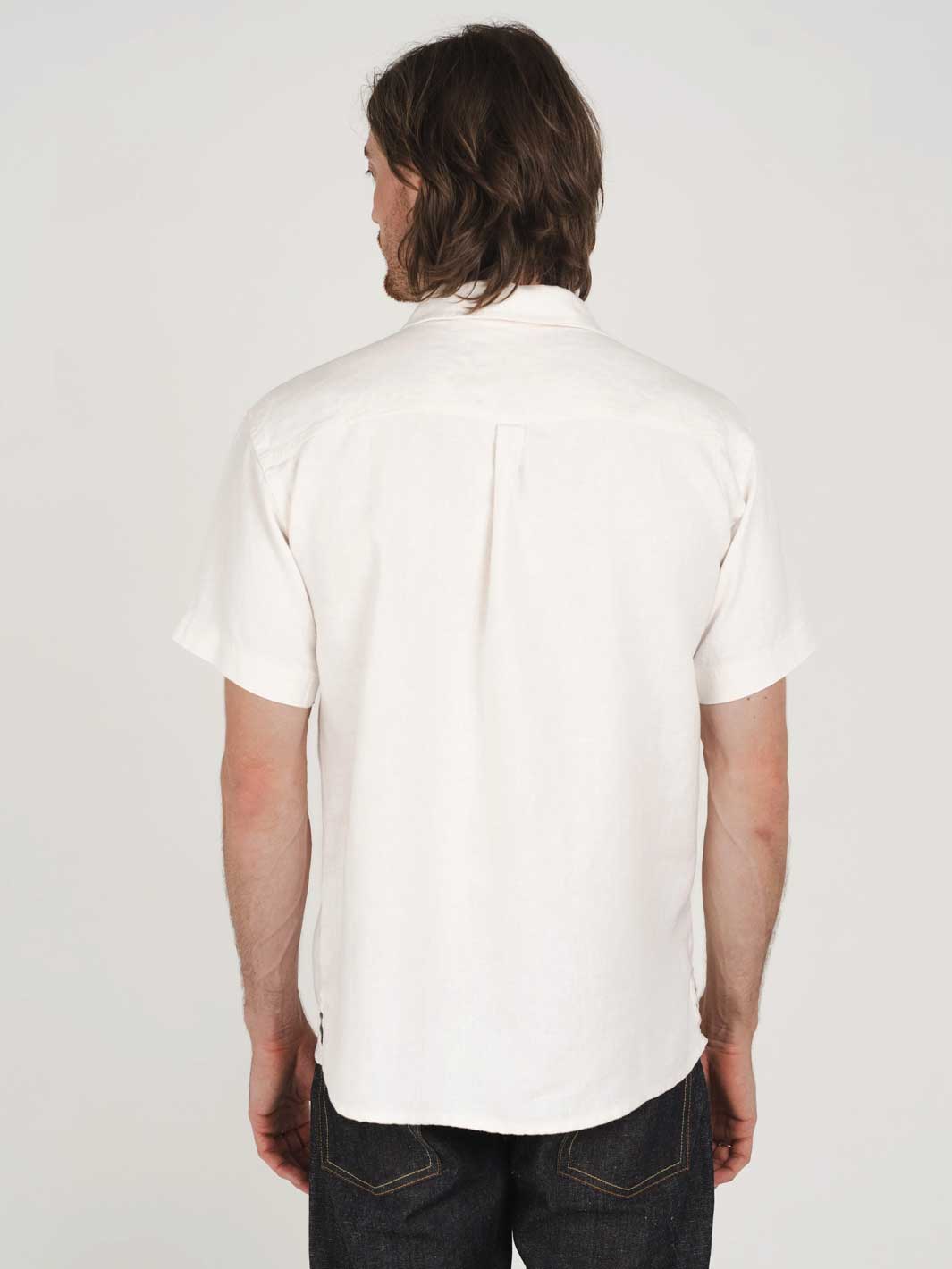 Person wearing a white hemp clothign Australia short-sleeve shirt and dark jeans on a plain background