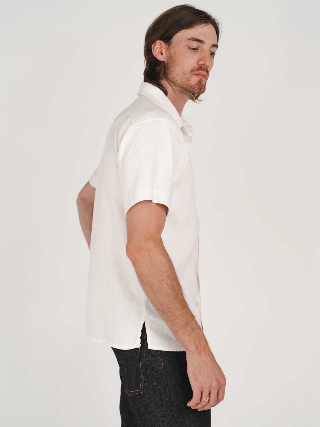 Man wearing a white hemp button up shirt and dark jeans against a plain background