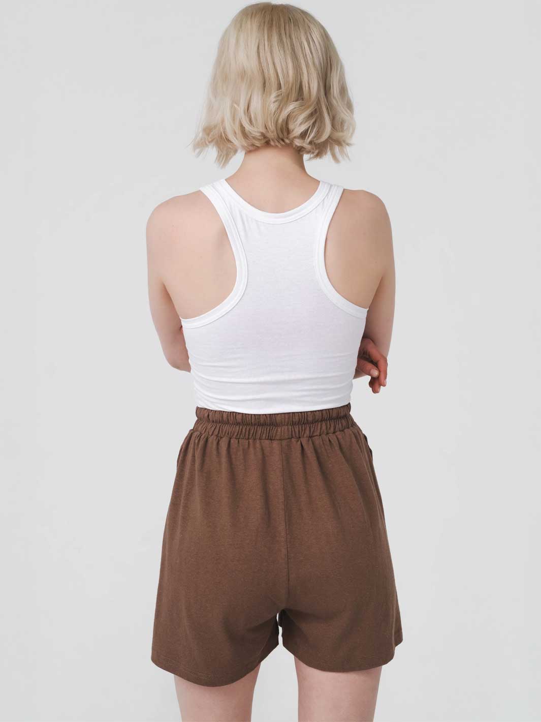 Person wearing a white tank top and brown shorts on a plain background