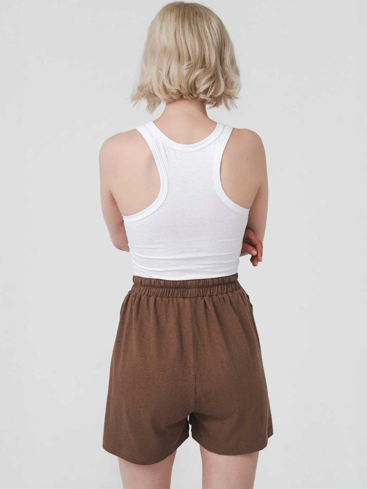 Person wearing a white tank top and brown shorts on a plain background