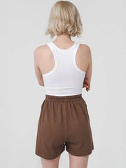 Person wearing a white tank top and brown shorts on a plain background