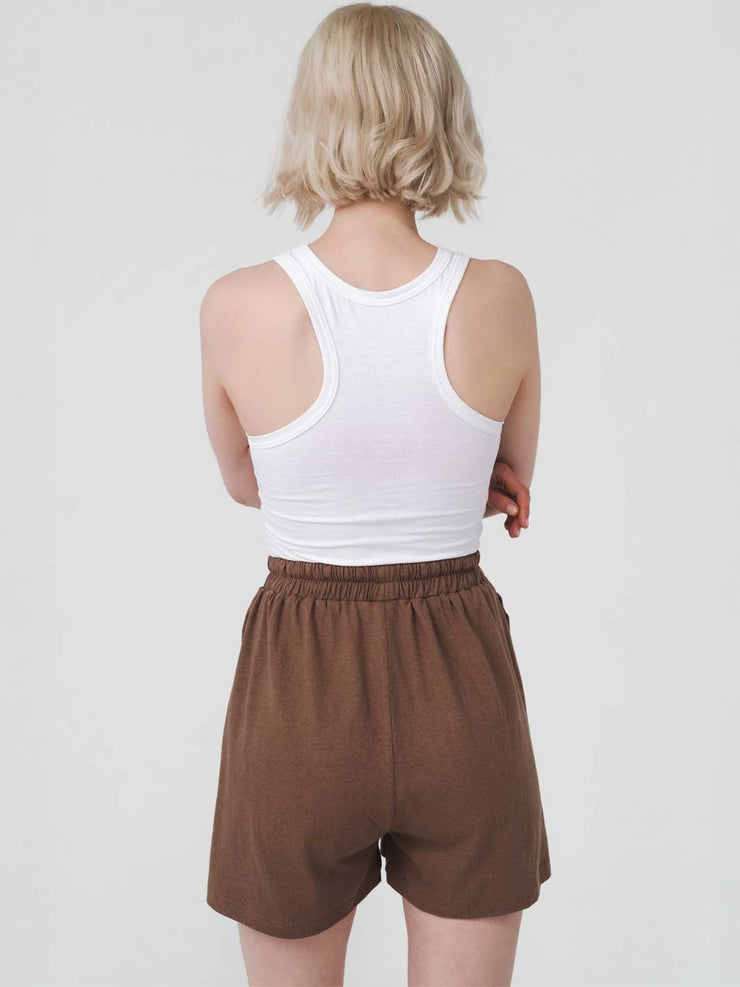 Person wearing a white tank top and brown shorts on a plain background