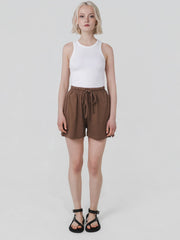 Person wearing a white sleeveless top and brown shorts on a plain background