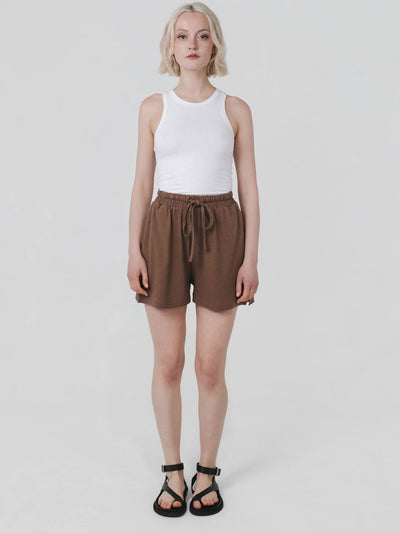 Person wearing a white sleeveless top and brown shorts on a plain background