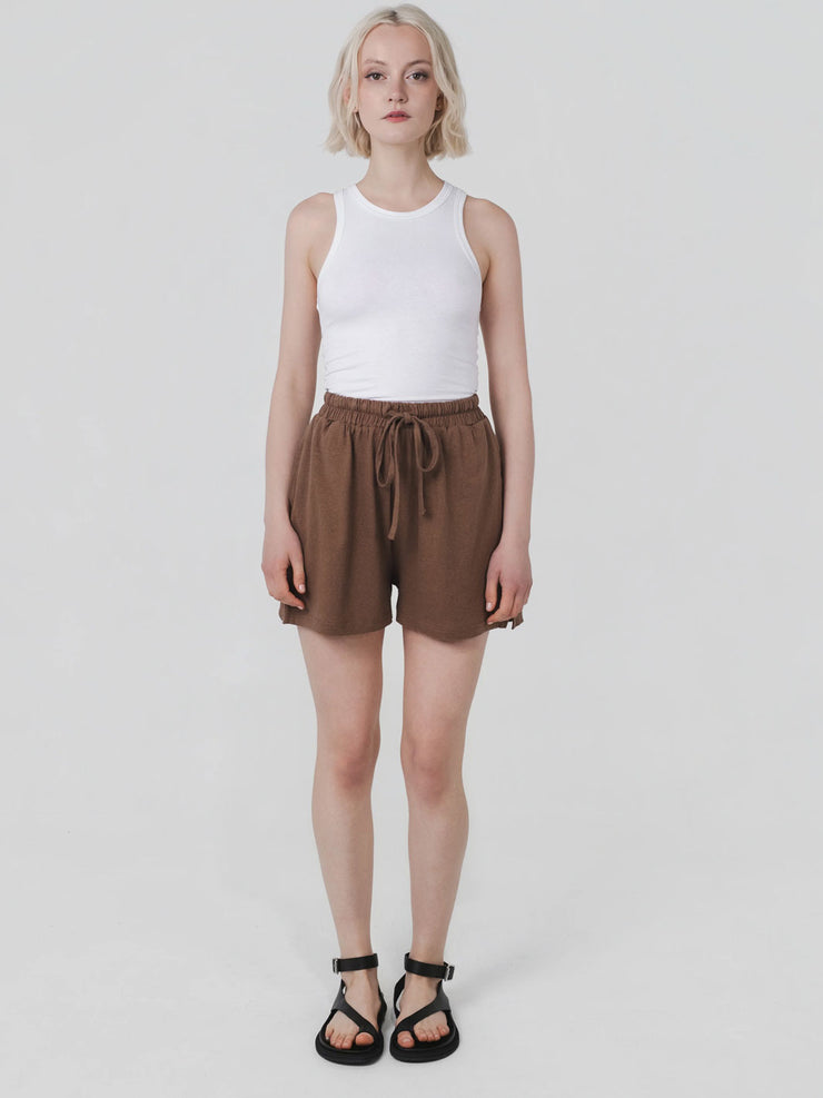 Person wearing a white sleeveless top and brown shorts on a plain background