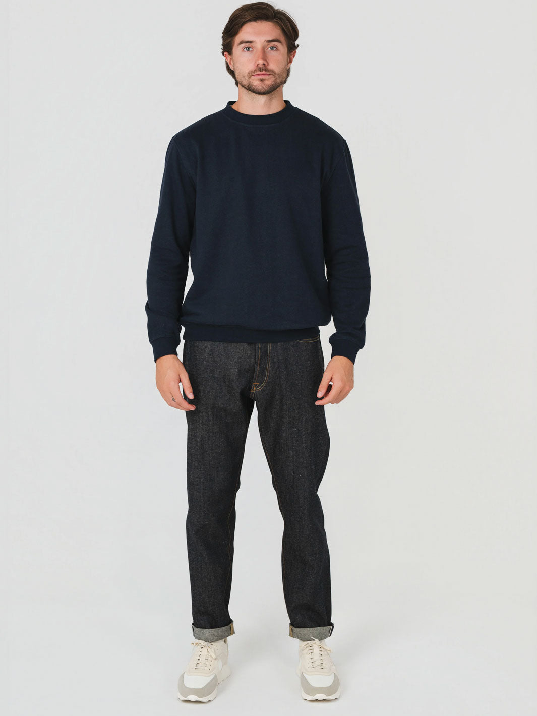 Man wearing a navy sweater and dark jeans on a white background