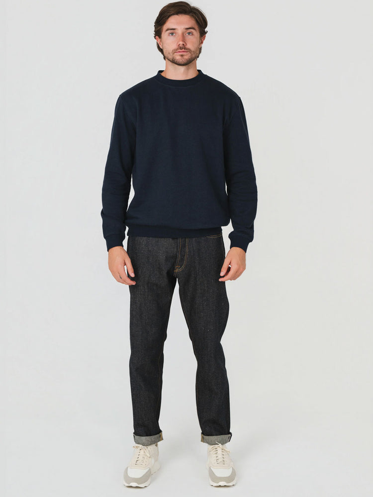 Man wearing a navy sweater and dark jeans on a white background