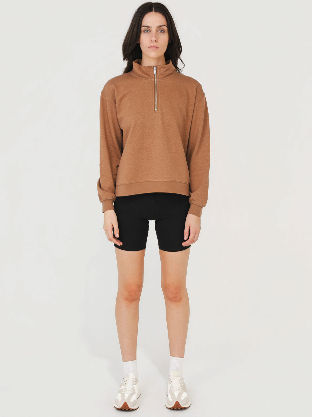 Woman wearing a brown sweatshirt and black shorts on a white background