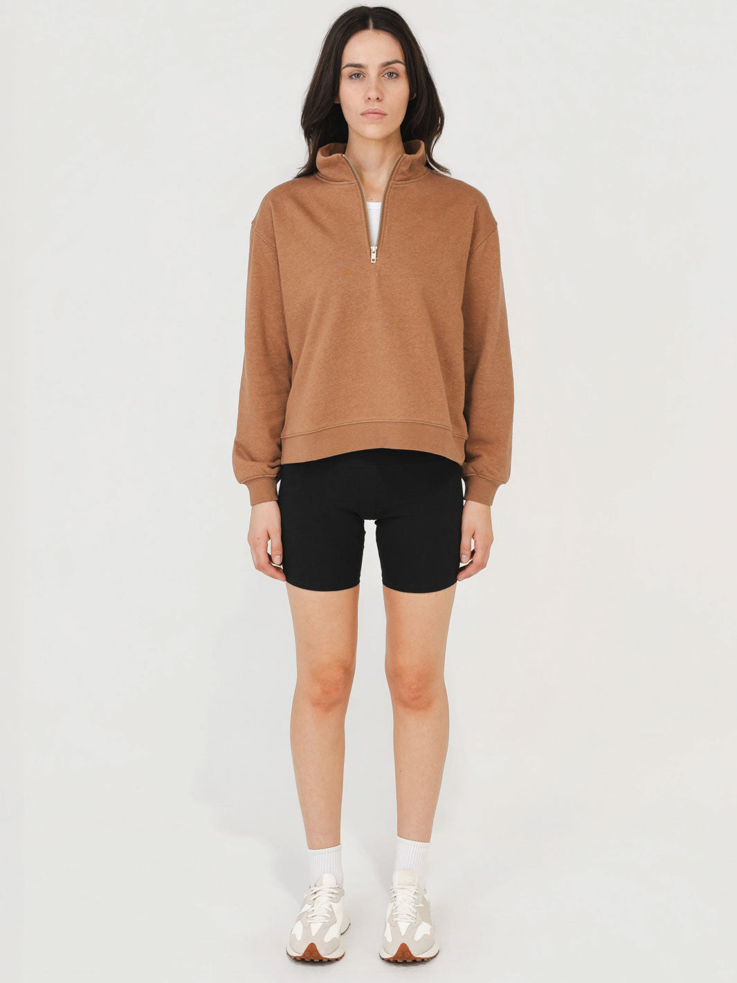 Woman wearing a brown zip-up sweatshirt and black shorts on a white background