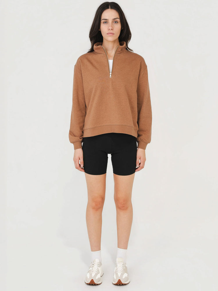 Woman wearing a brown zip-up sweatshirt and black shorts on a white background