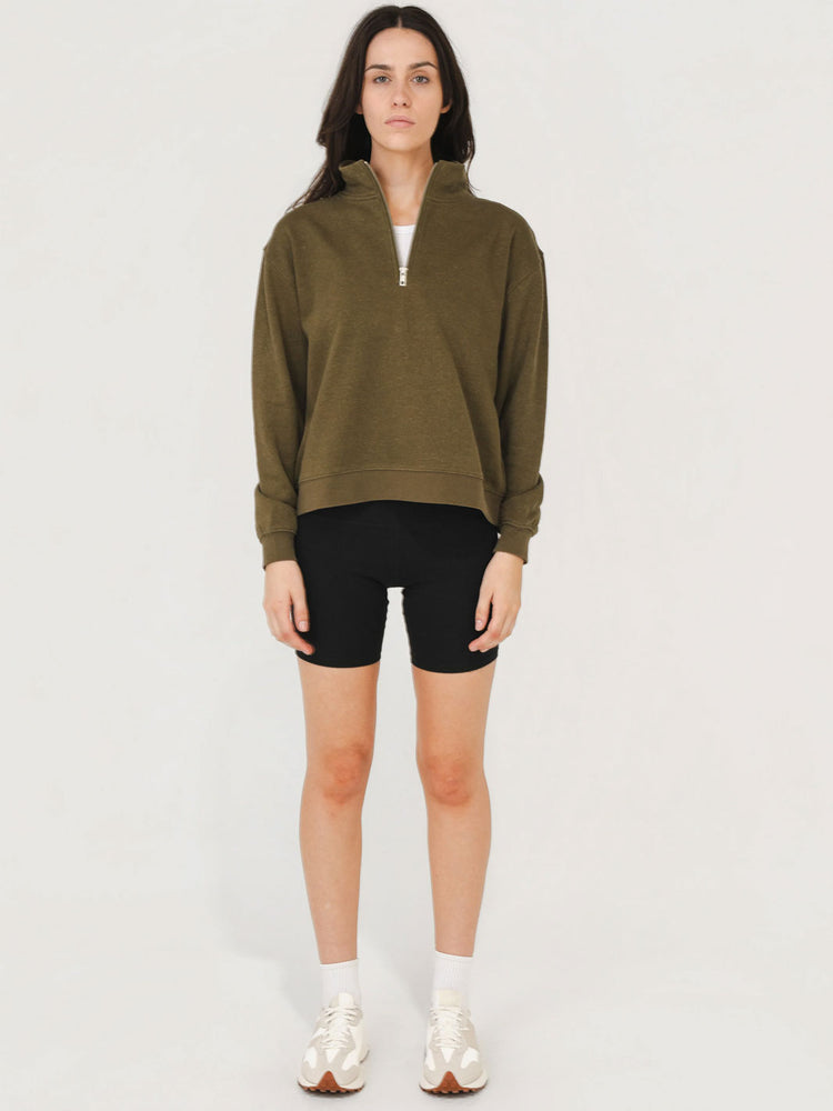 Woman wearing an olive green sweatshirt and black shorts on a white background