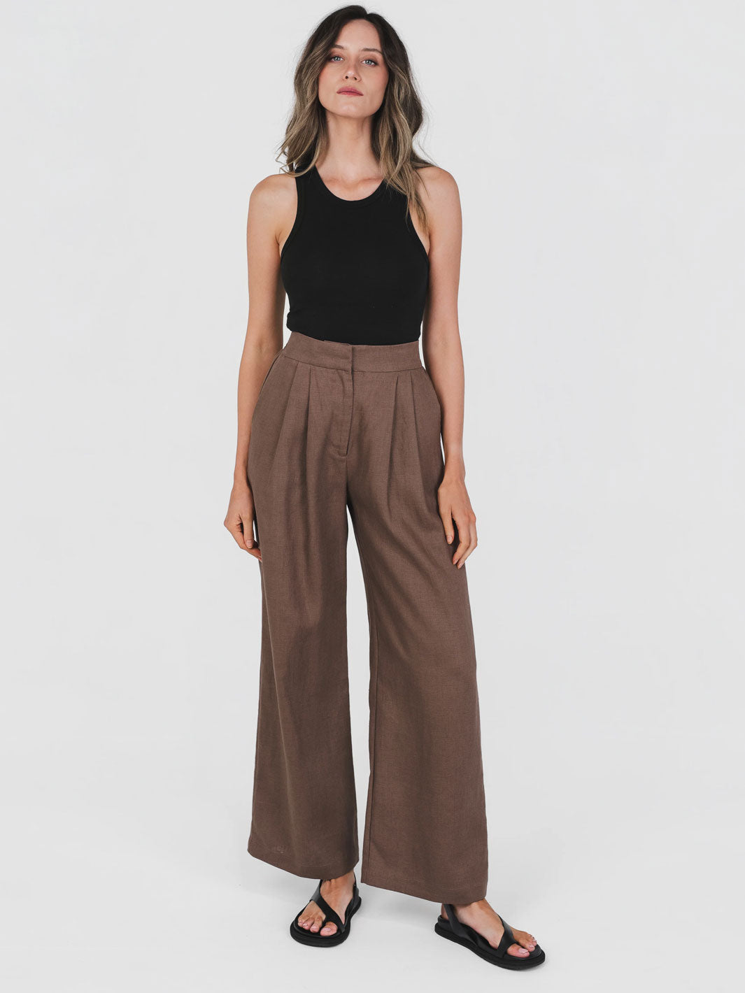 Woman wearing a black sleeveless top and brown wide-leg pants on a white background