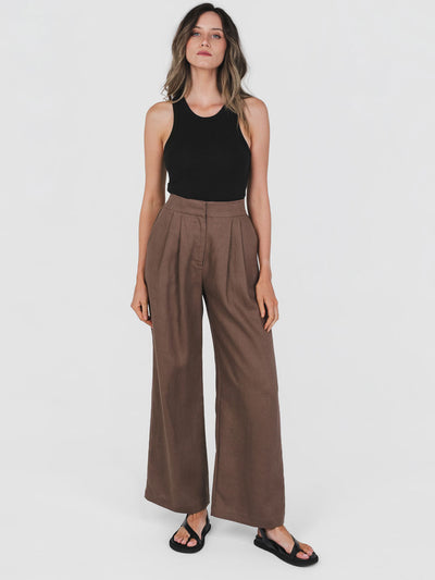 Woman wearing a black sleeveless top and brown wide-leg pants on a white background