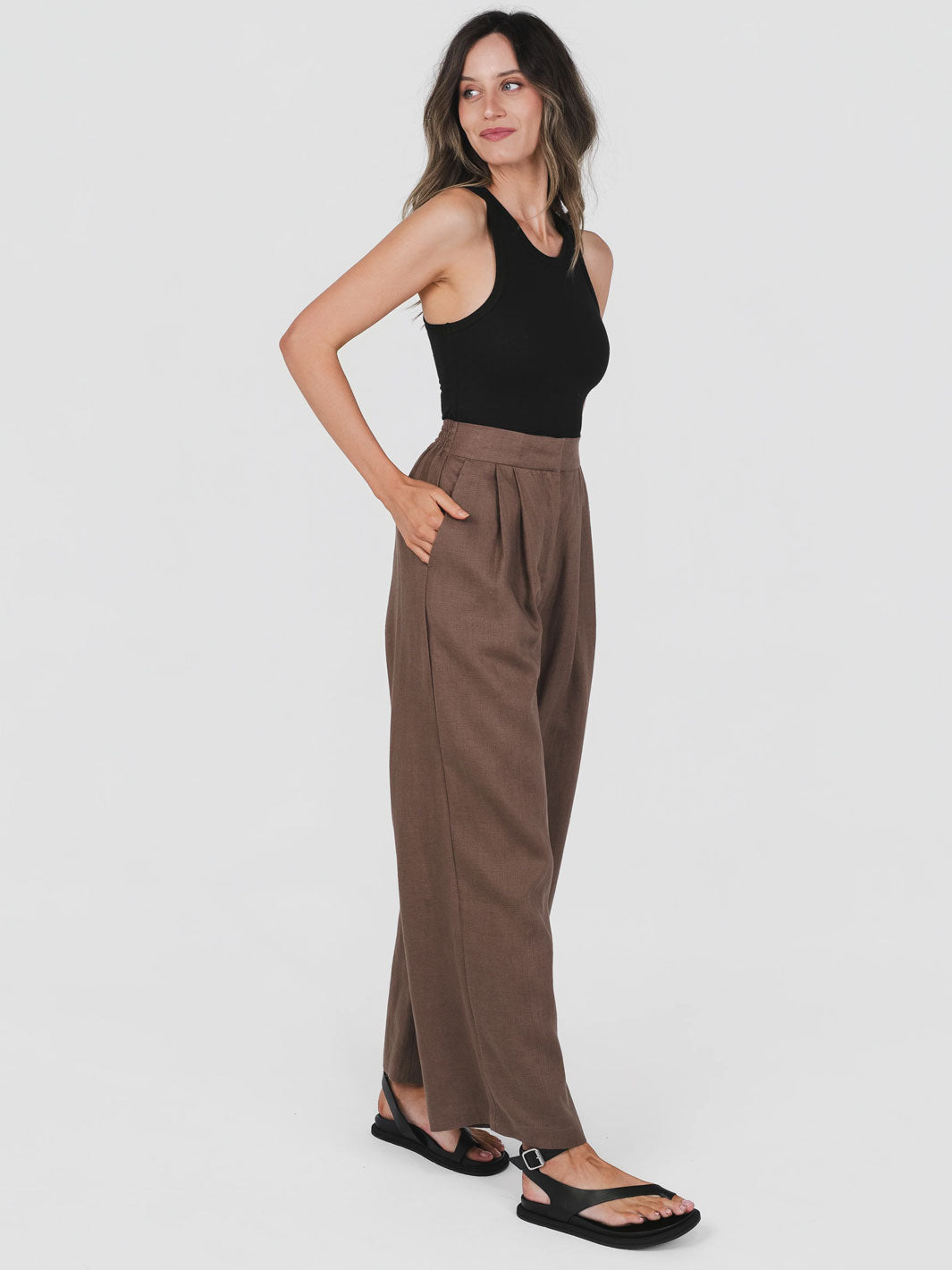 Woman wearing Hemp Clothing Australia brown tailored pants and a black top on a white background