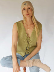 Woman wearing a green knitted vest, beige beanie, and light blue jeans against a white background