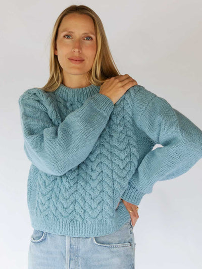 Woman wearing a light blue knitted sweater against a white background
