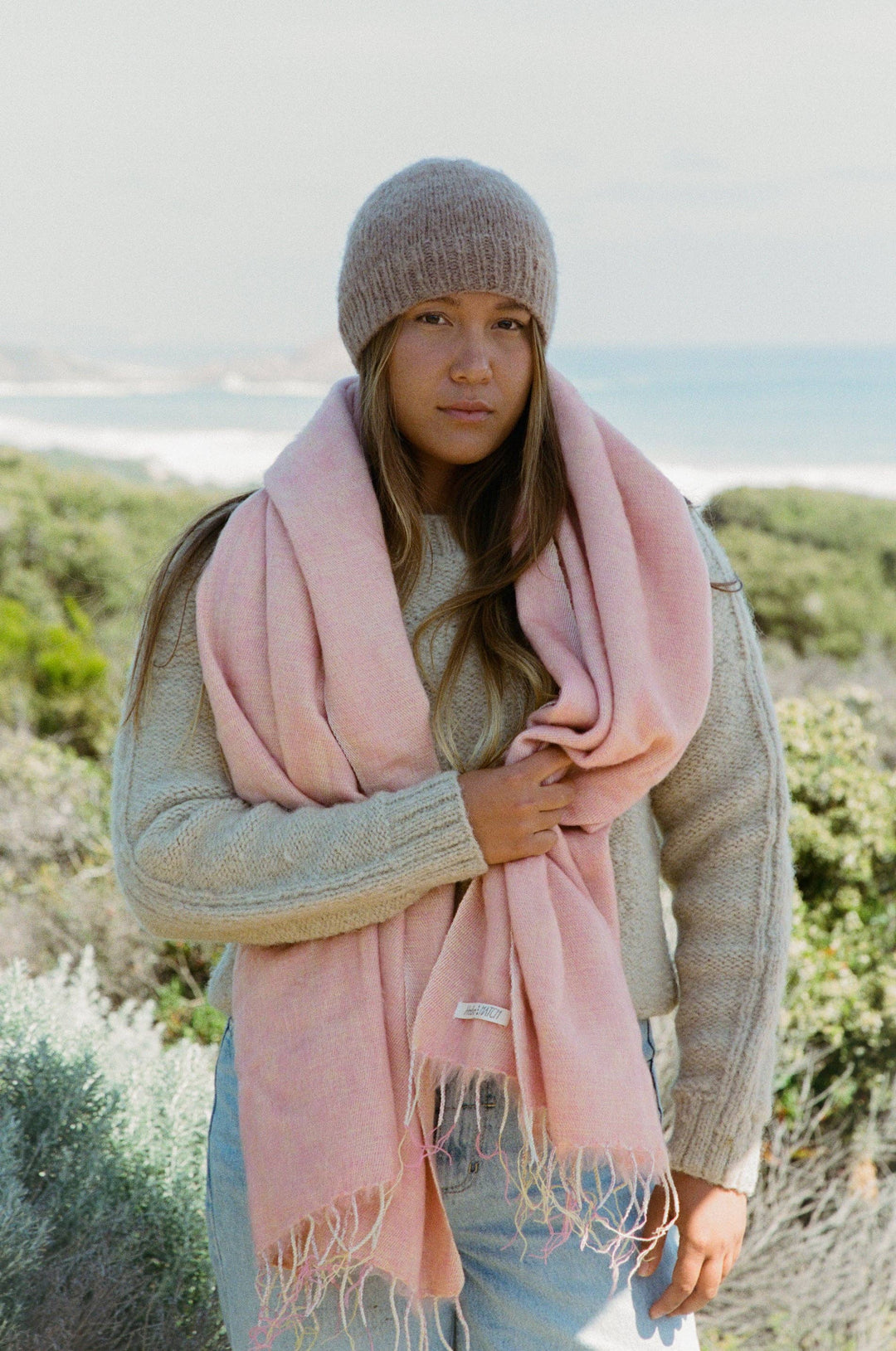 Woman wearing a pink scarf and knit hat outdoors with a scenic background
