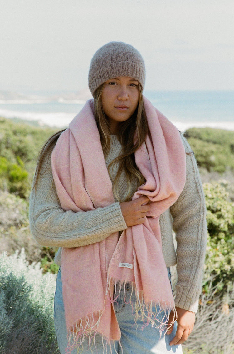 Woman wearing a pink scarf and knit hat outdoors with a scenic background