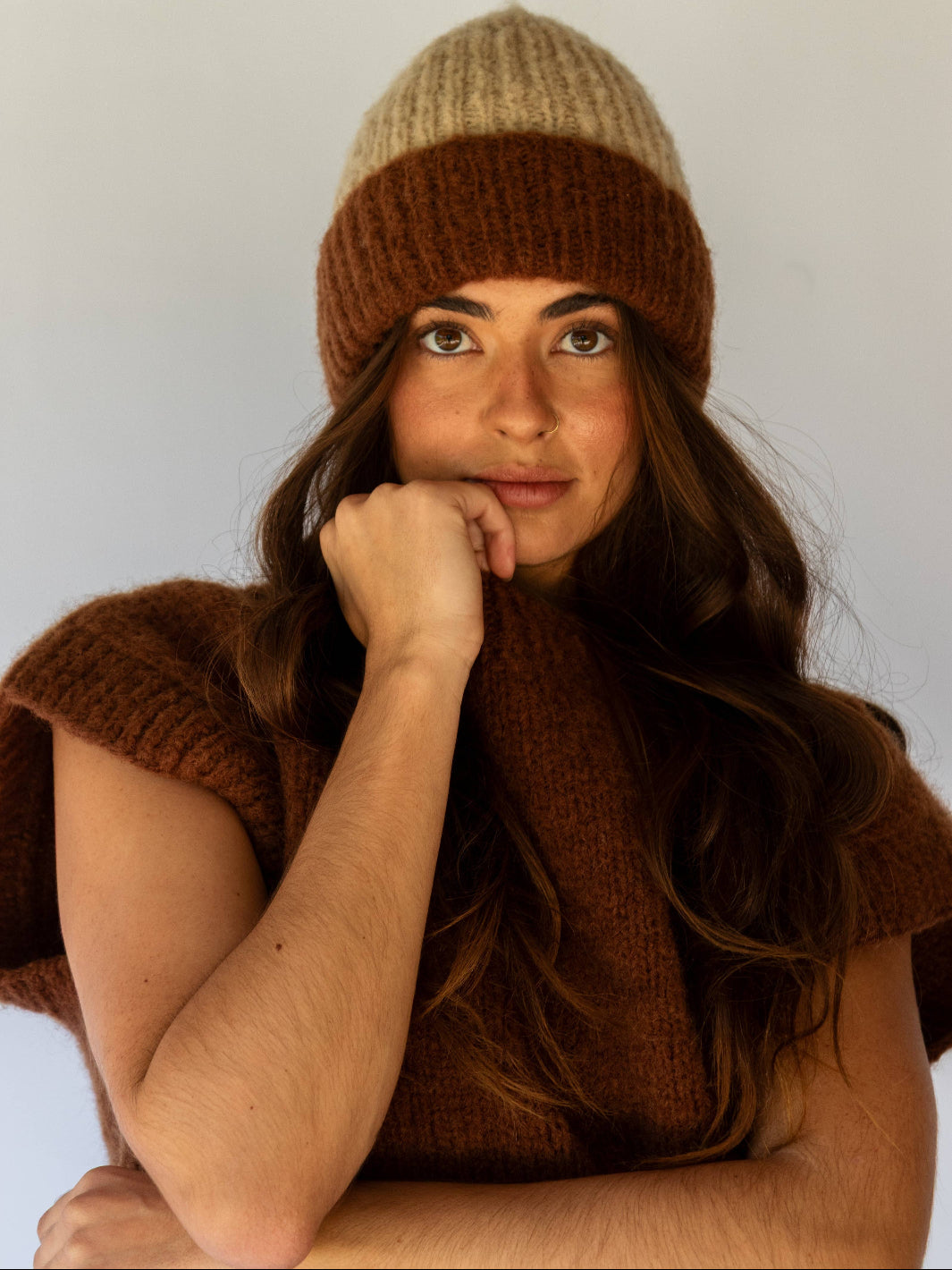 Woman wearing a brown knit hat and scarf against a plain background