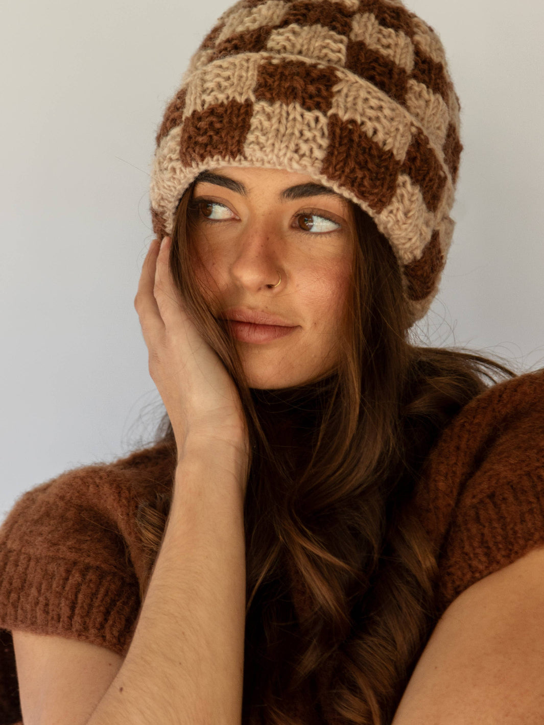 Woman wearing a checkered knitted hat and matching sweater against a plain background