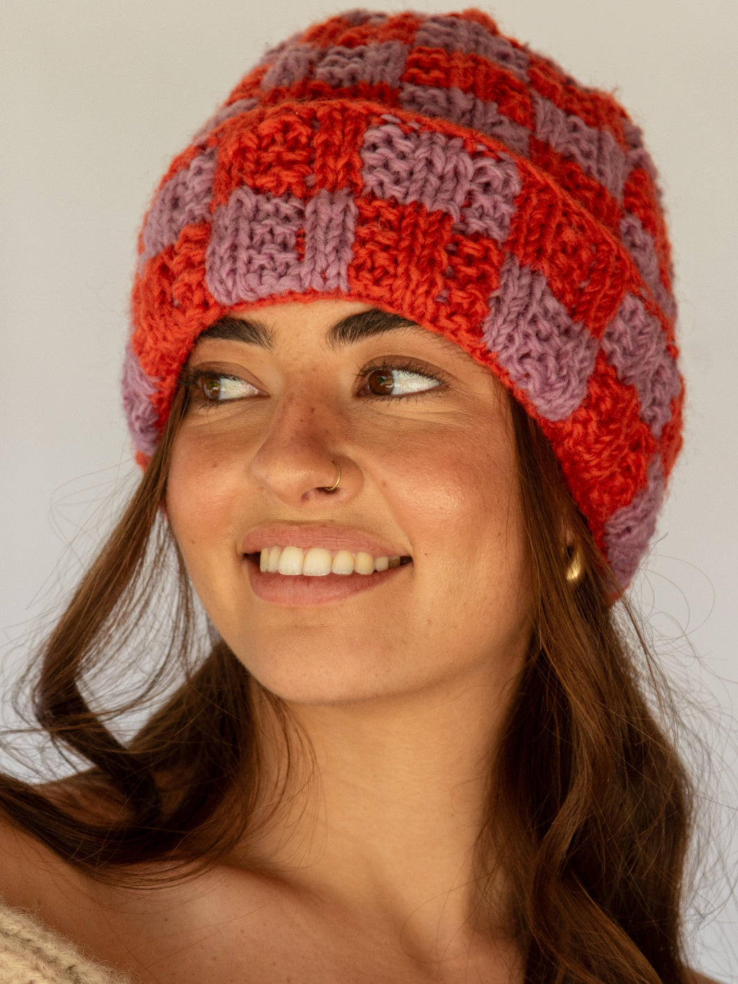 Woman wearing a red and purple checkered knit hat against a plain background