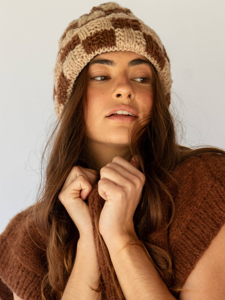 Woman wearing a knitted brown beanie and scarf against a plain background
