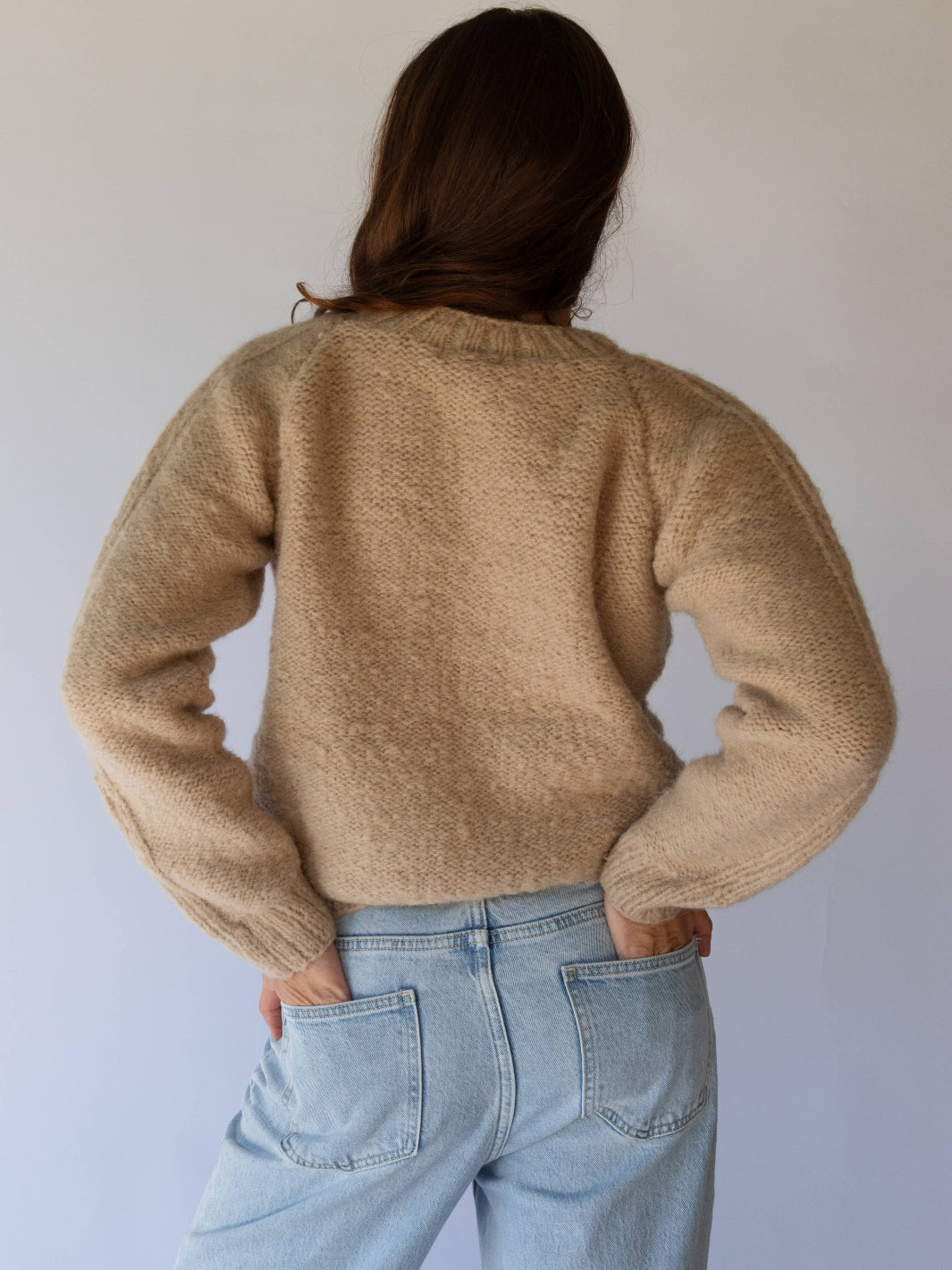 Person wearing a beige sweater and light blue jeans against a plain background