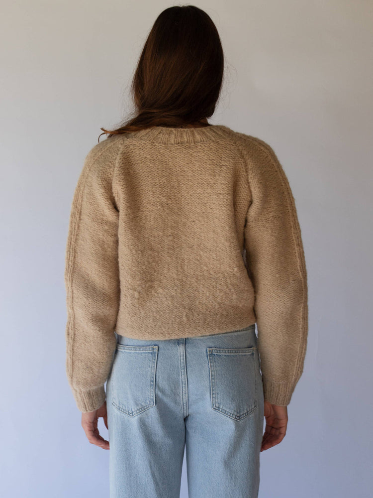Person wearing a beige sweater and light blue jeans against a plain background