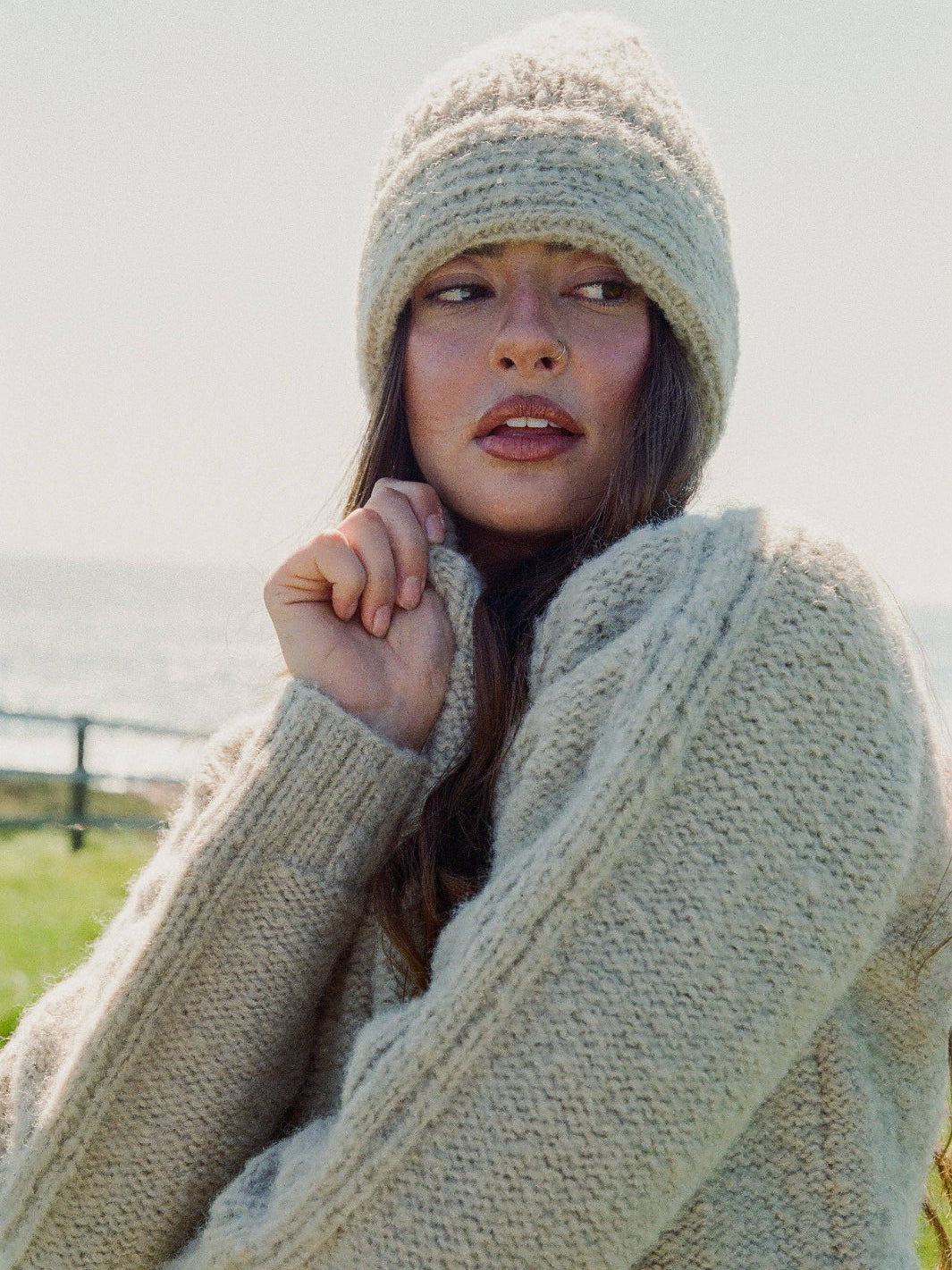 Woman wearing a beige knit sweater and hat outdoors with a blurred background