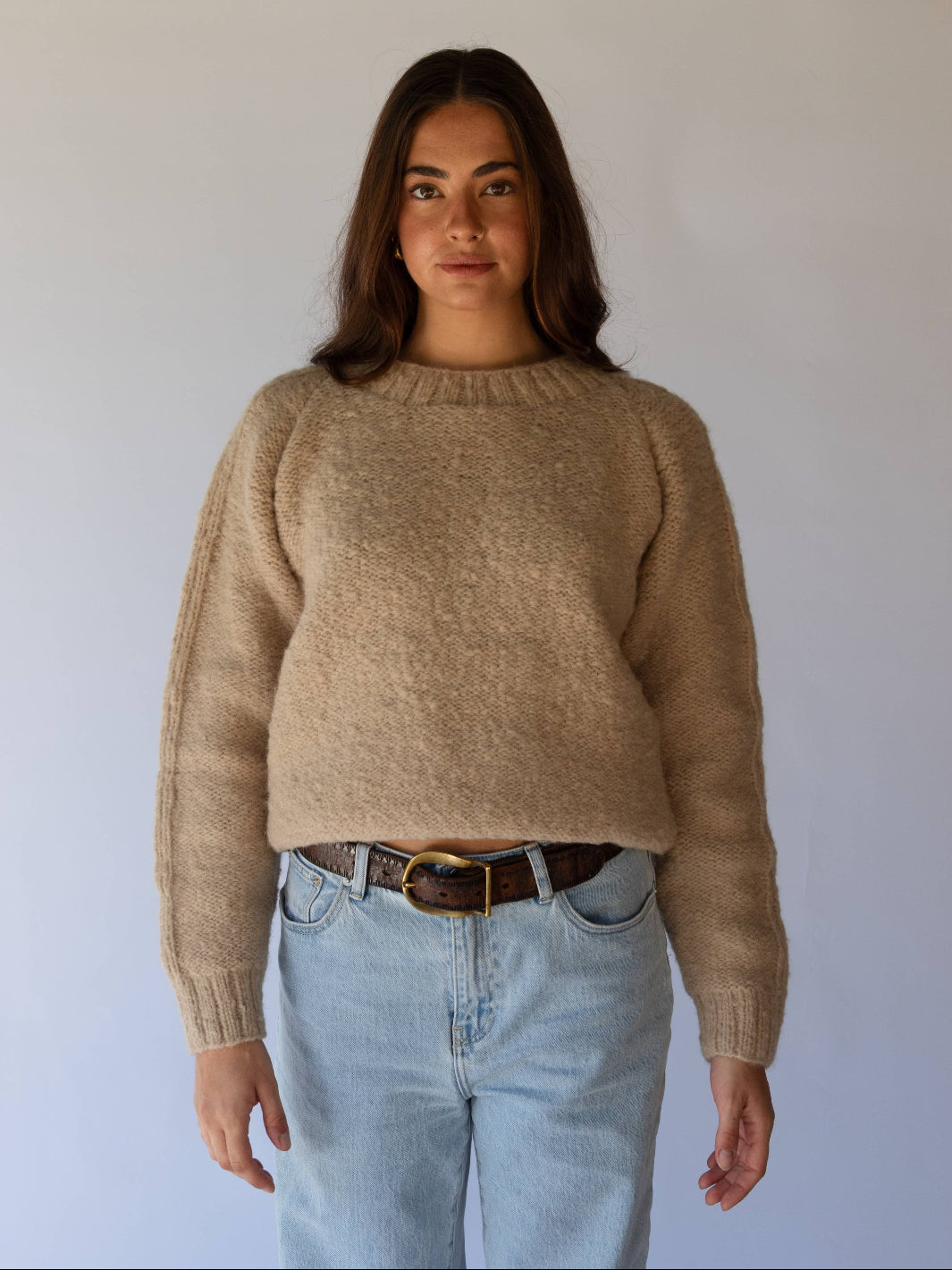 Woman wearing a beige sweater and light blue jeans against a plain background