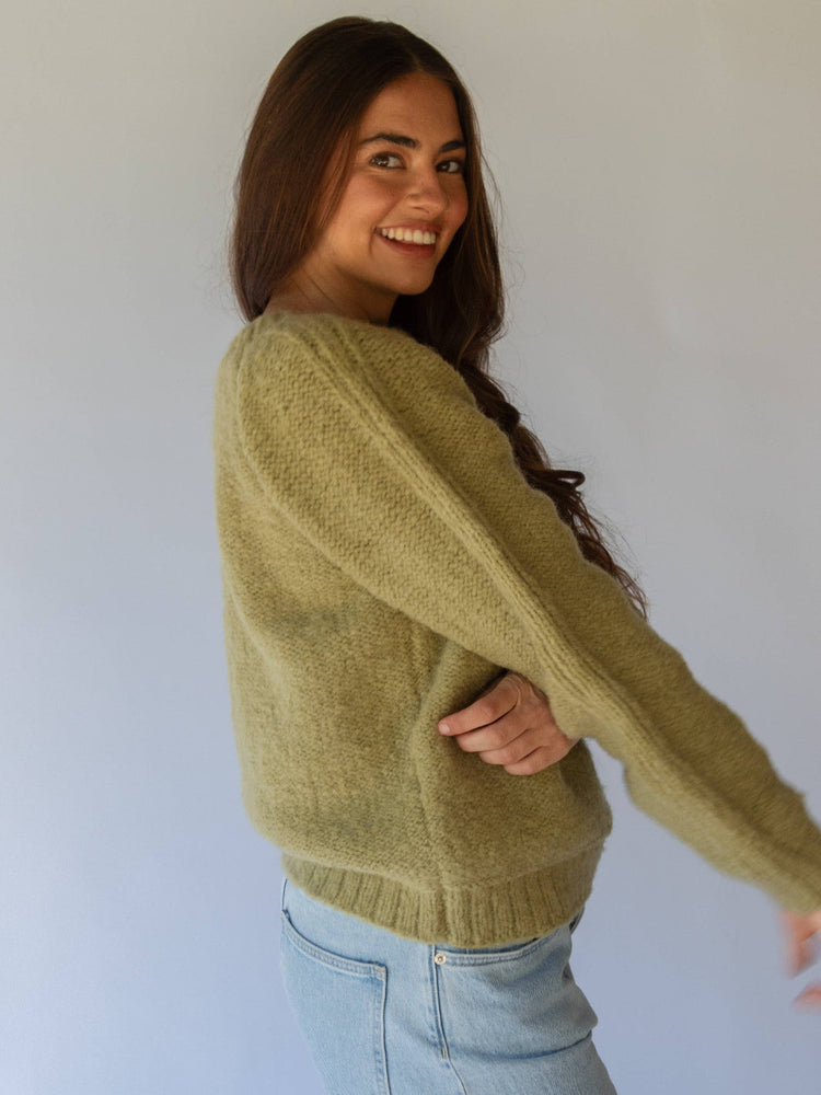Woman wearing a green sweater and blue jeans against a white background