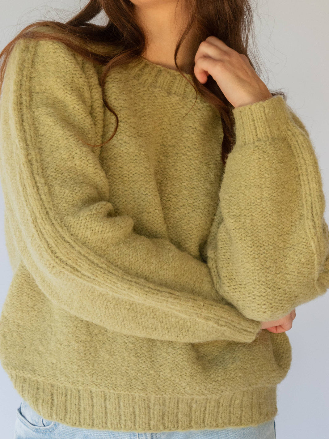 Person wearing a mustard greensweater against a white background