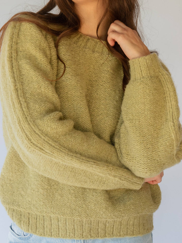 Person wearing a mustard greensweater against a white background