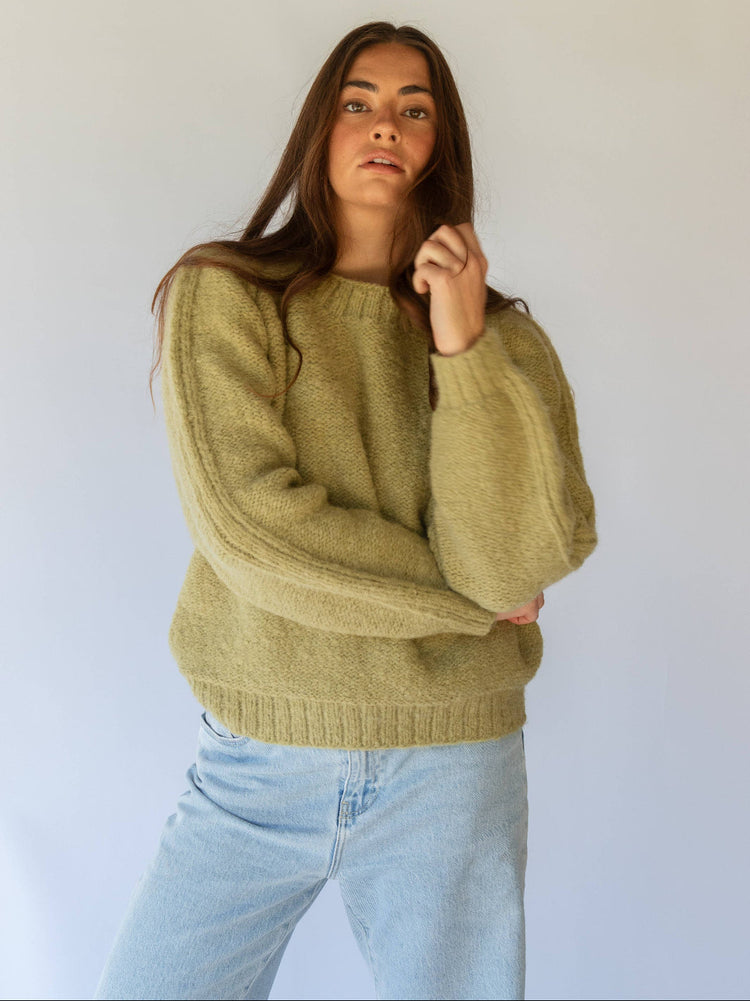 Woman wearing a green sweater and light blue jeans against a white background