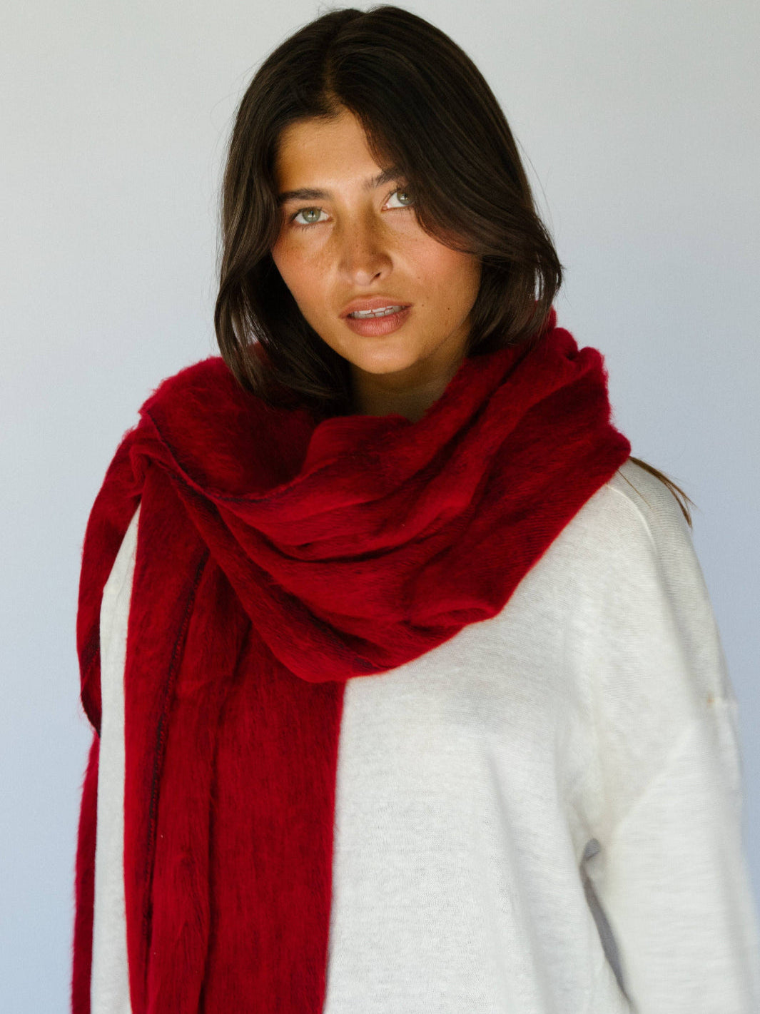 Woman wearing a red scarf and white sweater against a plain background