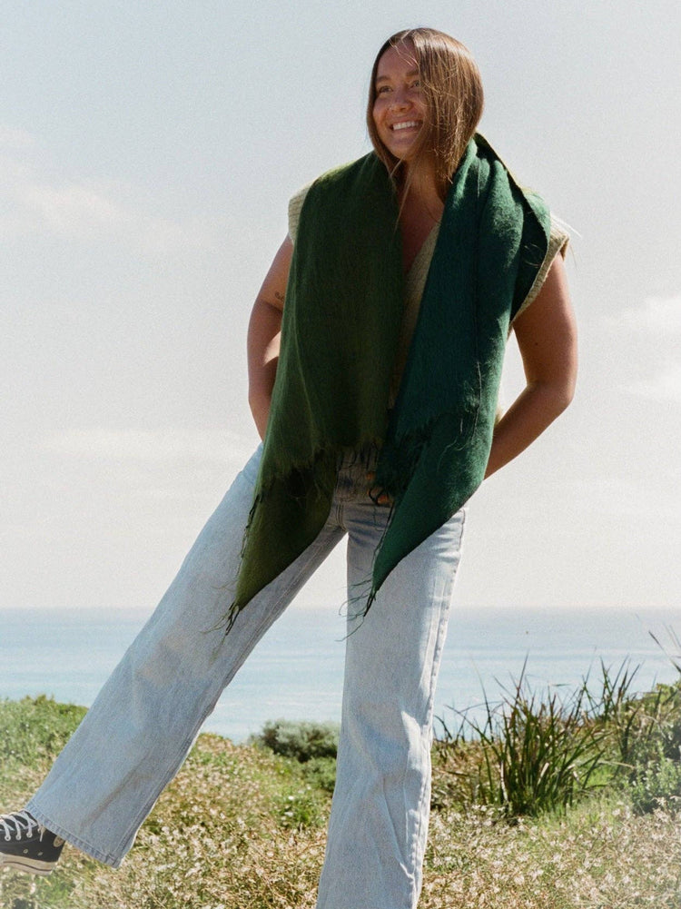 Woman wearing a green scarf and light-colored pants standing outdoors with a clear sky.