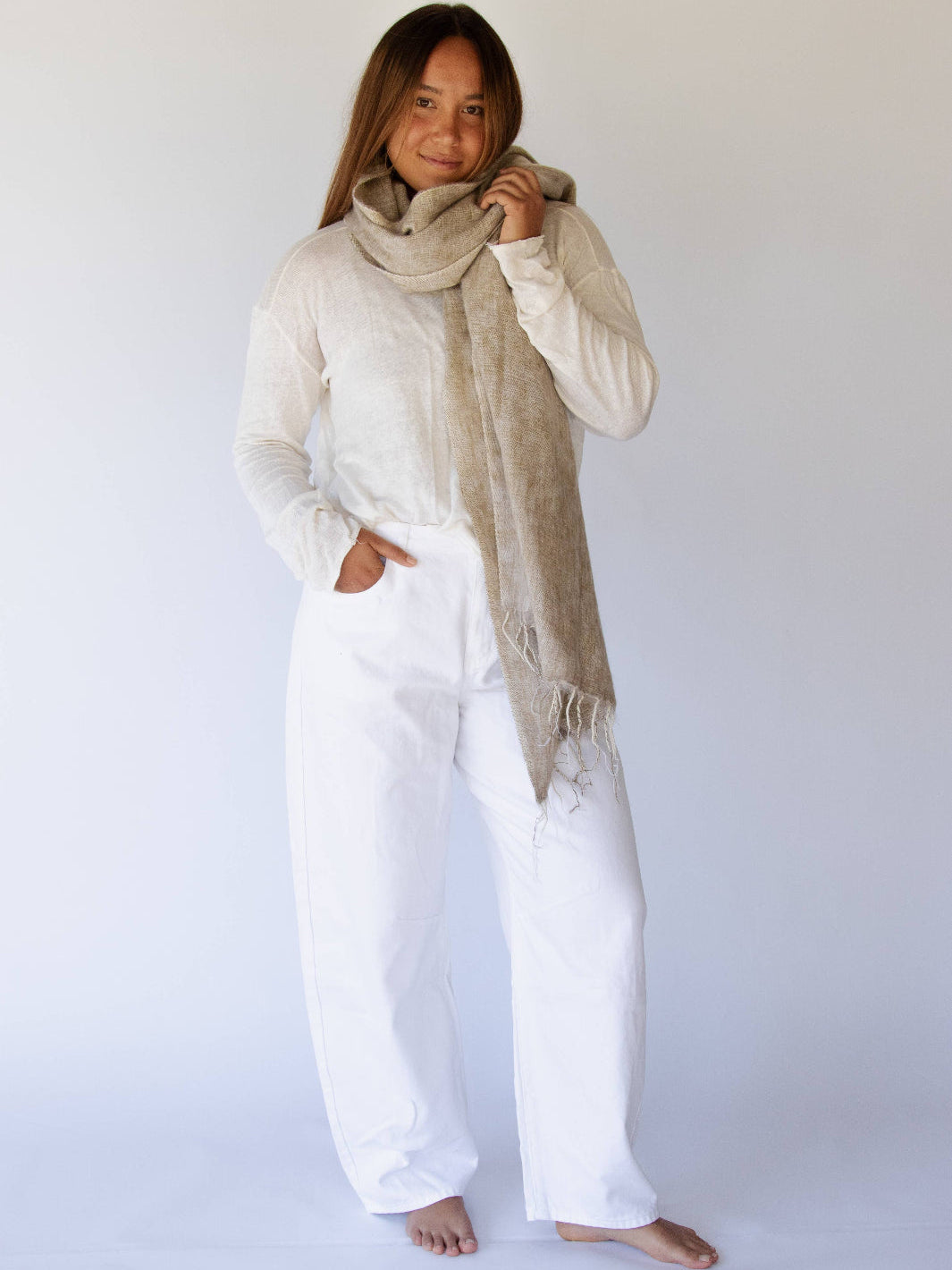 Woman wearing a beige scarf and white outfit against a plain background
