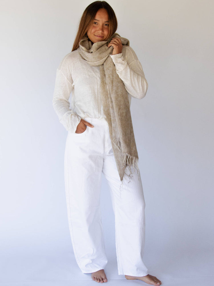 Woman wearing a beige scarf and white outfit against a plain background