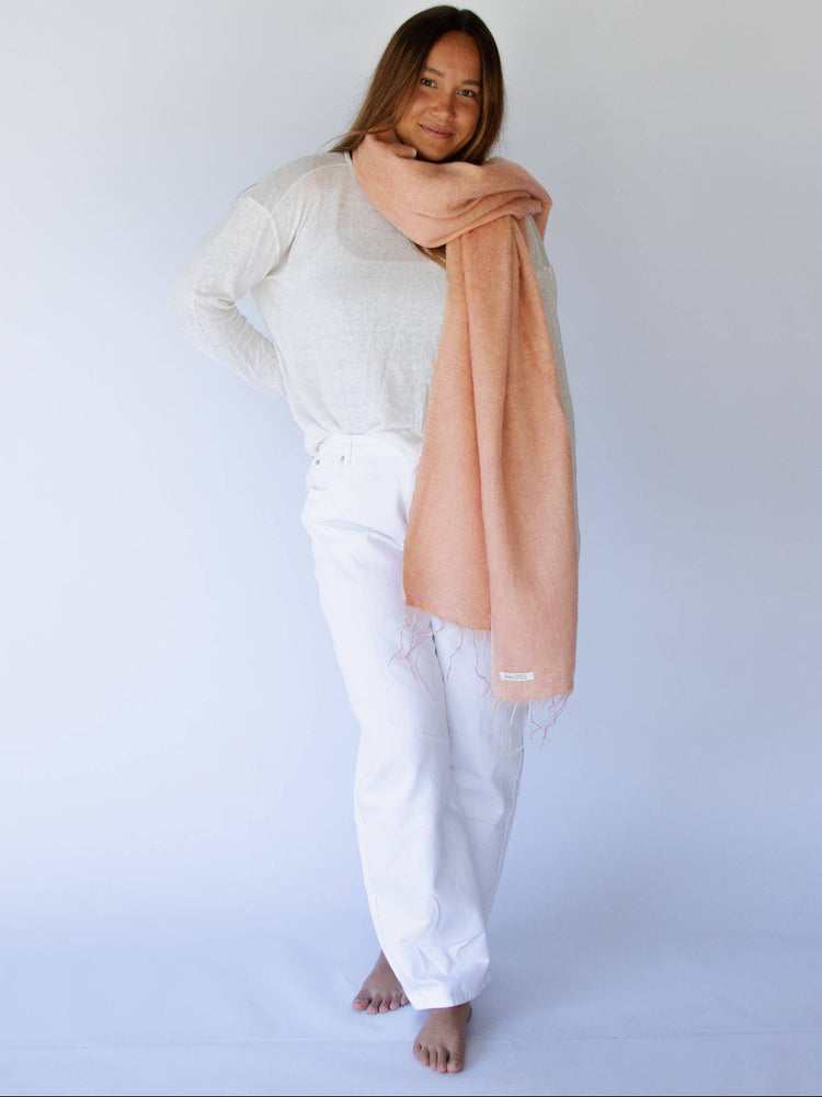 Person wearing a peach scarf and white outfit against a plain background