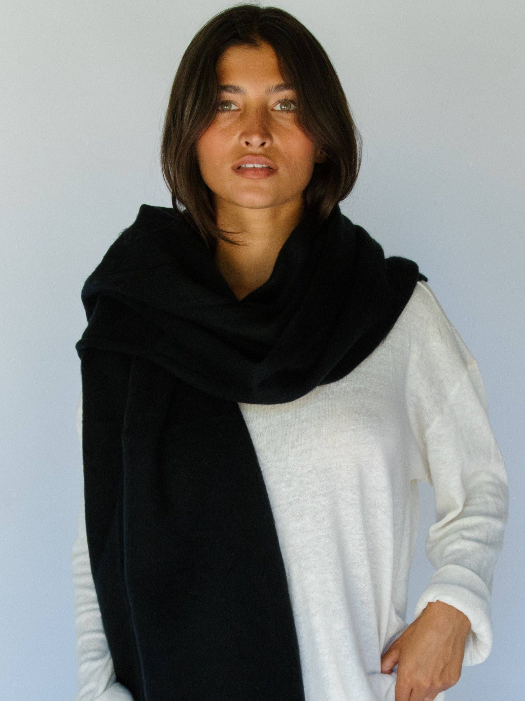 Woman wearing a black scarf over a white sweater against a light blue background