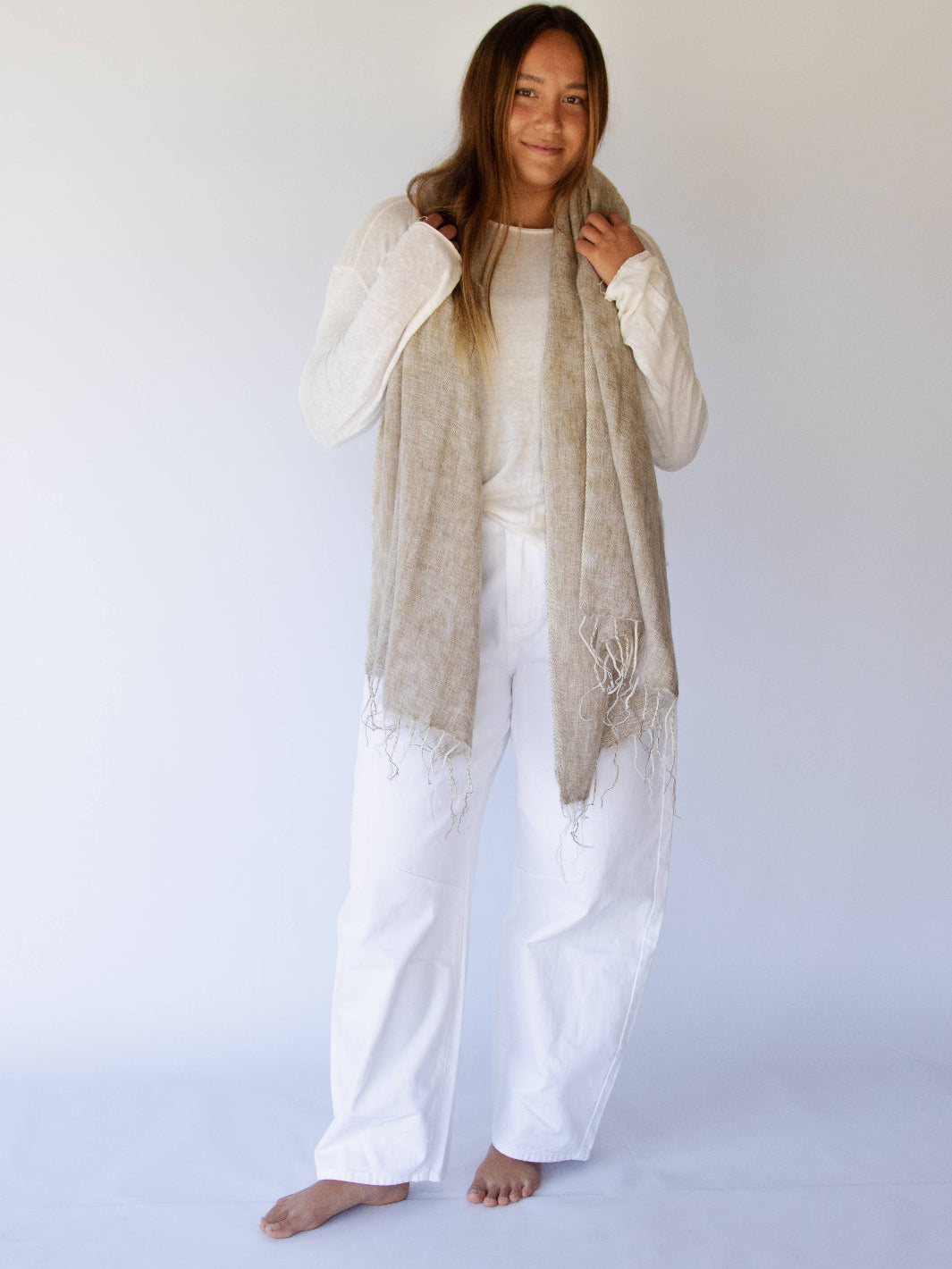 Woman wearing a beige scarf shawl over a white outfit on a plain background