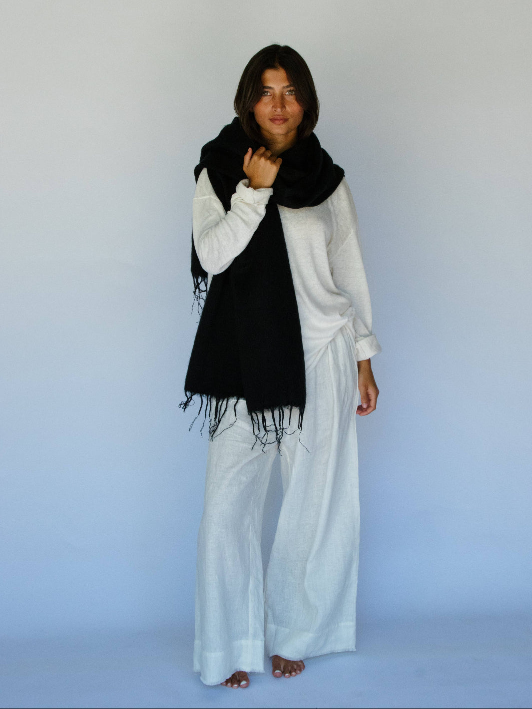 Person wearing a black scarf and white outfit against a light blue background