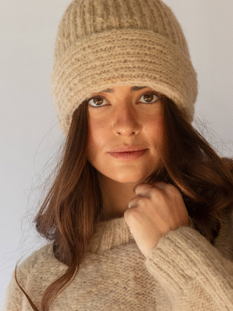 Woman wearing a beige knitted hat and sweater against a plain background