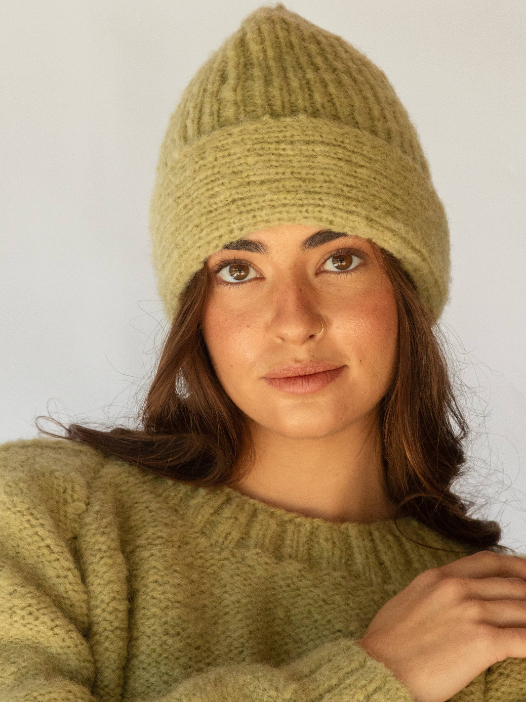 Woman wearing a green knit sweater and hat against a plain background