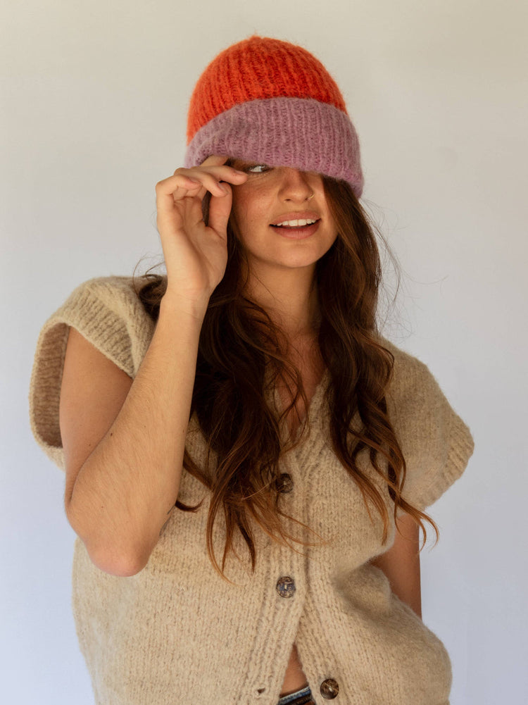 Woman wearing a two-tone knit hat and beige cardigan against a white background